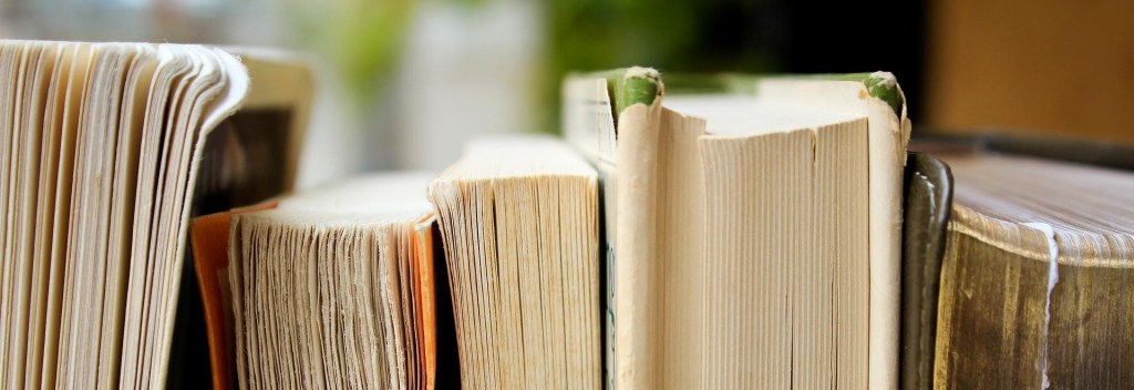A row of well-loved books with creamy-colored pages and covers in shades of green and orange.